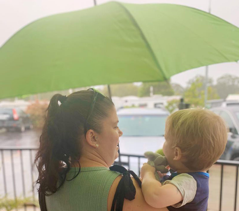 Mum holds an umbrella over babies head. Kindnesses, like umbrellas on wet days, can spark conversations and encourage family engagement.