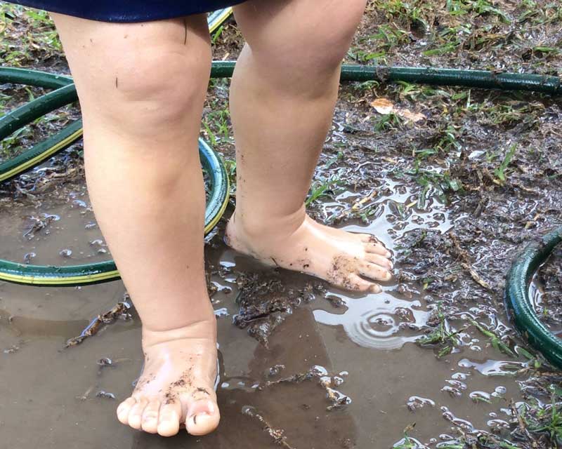 Child playing outside in muddy puddles on rainy days.