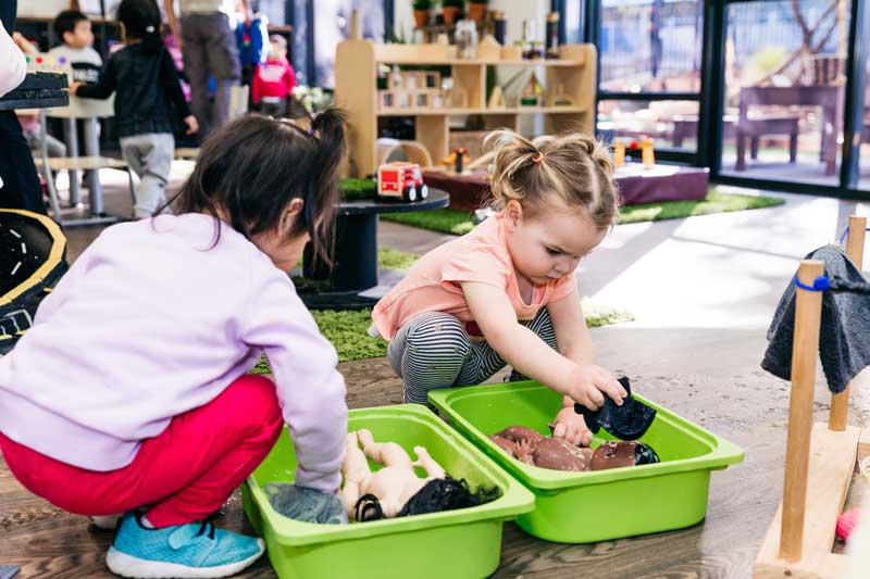 Children engage in pretend play as mothers bathing babies.