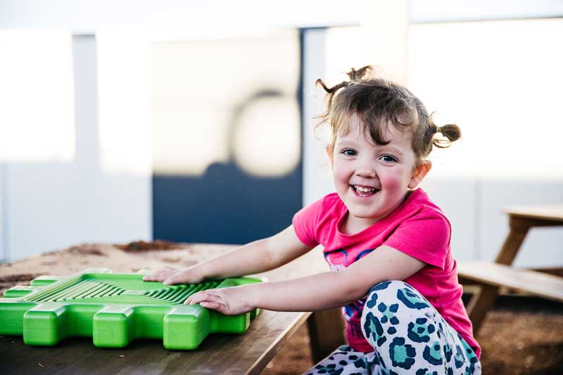 Child grabs a green puzzle mat where sorting colours can make cleaning fun.