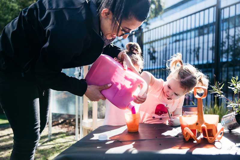 Educator pours paint for children doing sand painting.