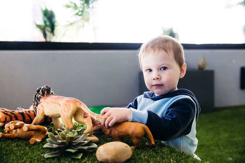 Child stands at a discovery station themed with animal toys and natural things for baby playtime.