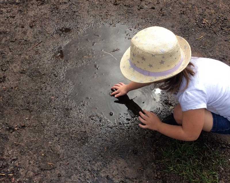 Child explores a muddy puddle for a rainy day activity.