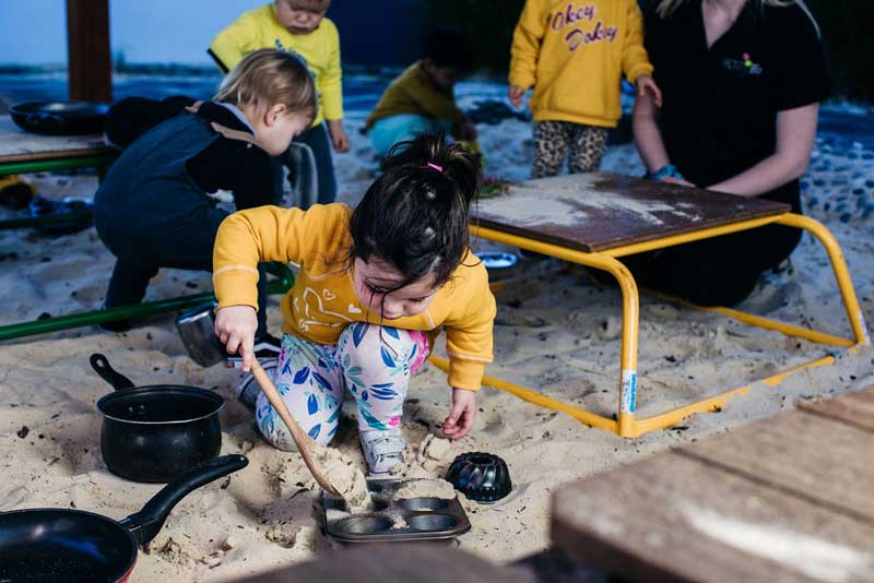 A child self-directs play in a sand kitchen. A teaching strategy in early childhood education.