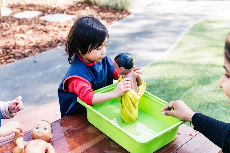 Child practises bathing a doll while learning about basic hygiene practices in child care.