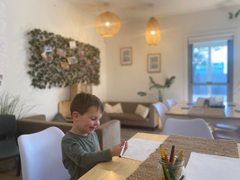 Child sits at desk with art. The soft furnishings engage families in children's learning.