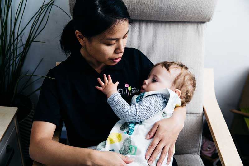 Educator makes eye contact while comforting a baby - a secure, respectful and reciprocal relationship example.