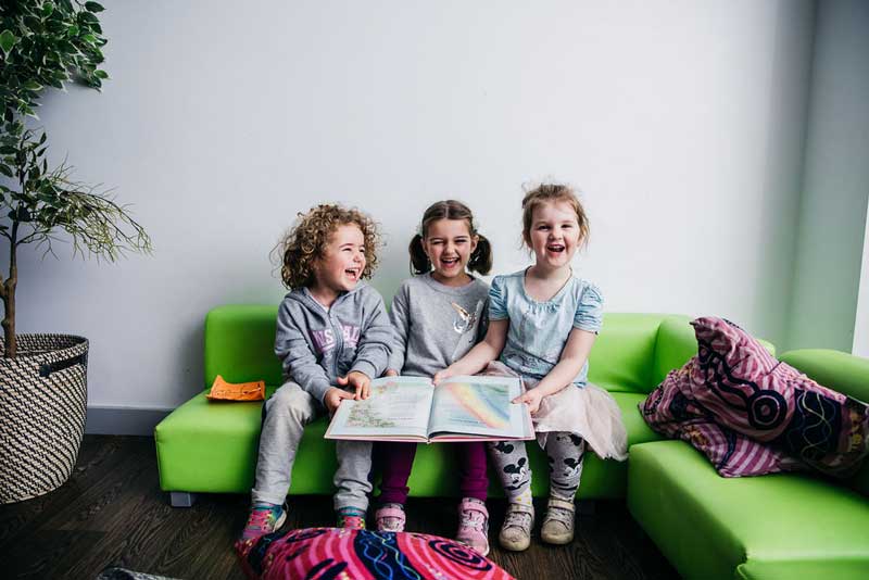 Three children laughing, share one book together. Sharing helps teach empathy to children.