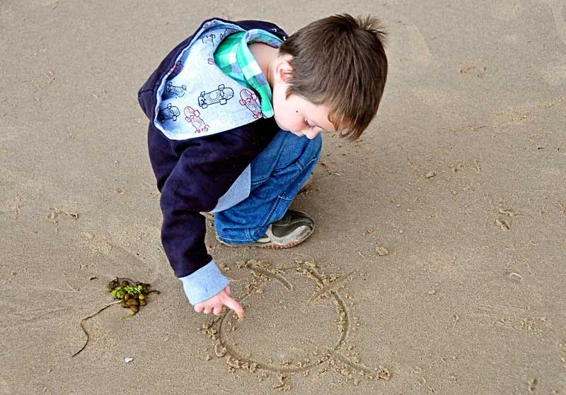 Child draws creative sand art with one finger.