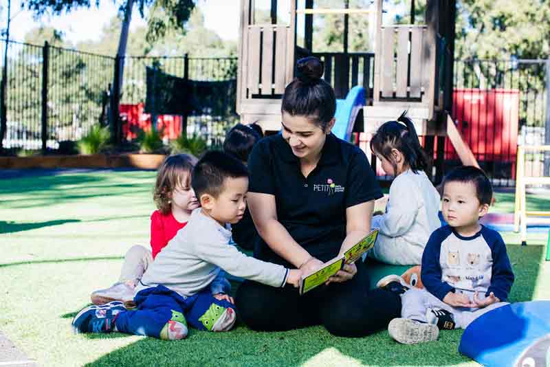 An Early Childhood Teacher reads to children outdoors.