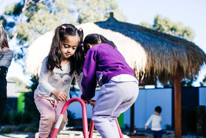 Teaching children kindness: Two children help each other navigate a climbing activity.