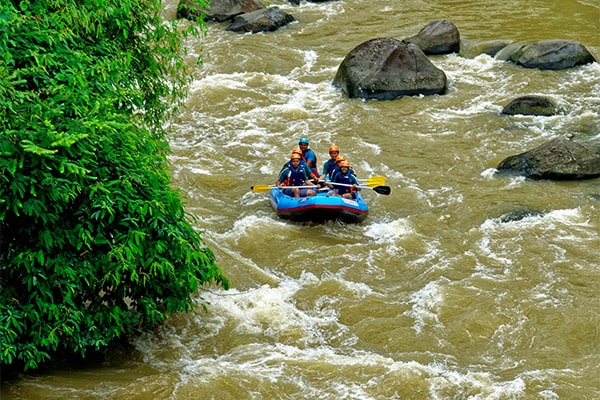 An adventure travel package showing a group of trekkers with backpacks navigating a suspension bridge over a river in the Himalayas.
