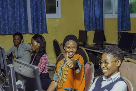 Des jeunes étudiants en salle d'informatique l'une souriante le pouce levé