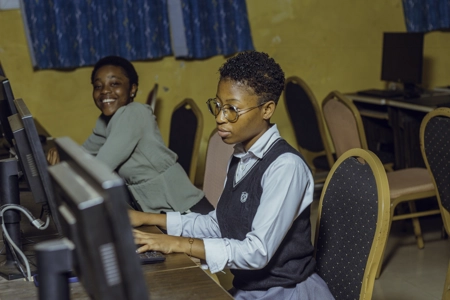 Deux jeunes étudiants en salle d'informatique l'une concentrée l'autre souriante