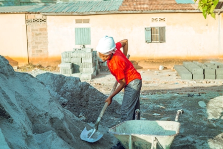 femme chef maçon sur un  chantier replissant une brouette de sable