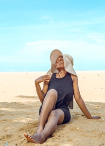 Femme souriante en bordure de plage evec un chapeau de soleil