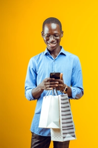 Homme souriant portant des avec son téléphone et des sacs de shopping