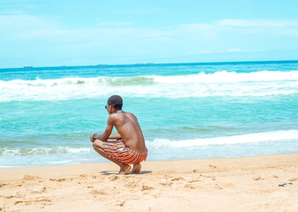 jeune homme accroupi en bordure de mer contemplant le paysage