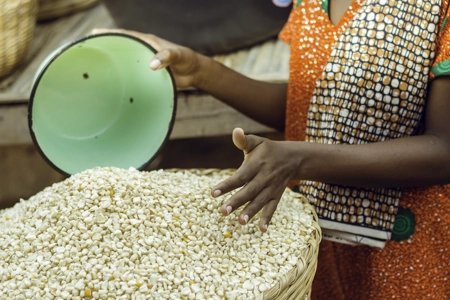 Une commerçante debout près de sa marchandise de maïs tenant un bol