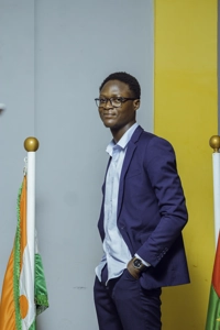 Une étudiant avec des lunettes et les mains dans la poche debout au milieu des drapeau