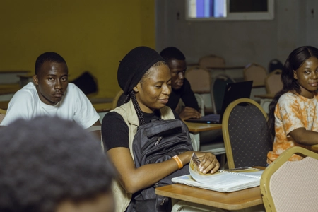 Une étudiante assise en classe parmi ses camarade ouvrant son livre