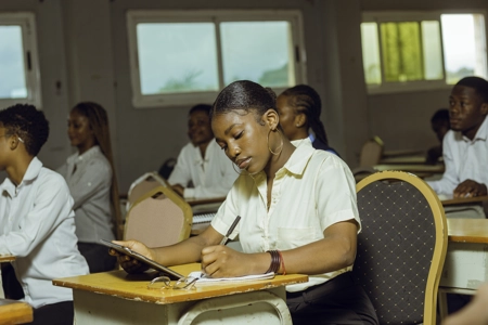 Une étudiante assise en classe tenant une tablette et écrivantt