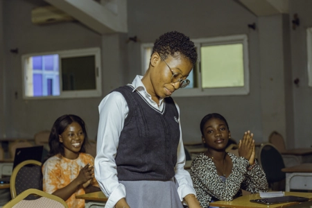 Une étudiante avec des lunettes debout en classe acclamée par ses camarades