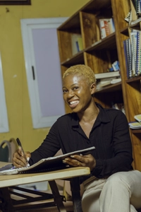 Une étudiante souriante assise dans la bibliothèque écrivant dans son cahier