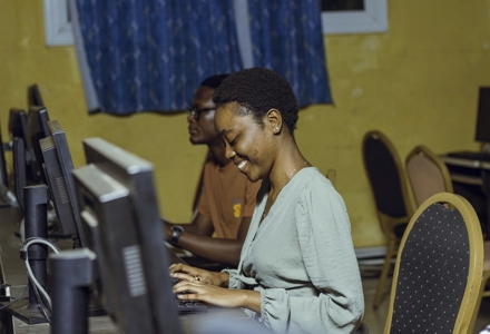Une étudiante souriante en salle d'informatique travaillant sur son ordinateur