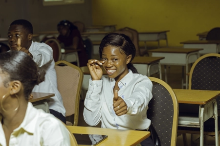 Une jeune étudiante souriante assise en classe le pouce levé