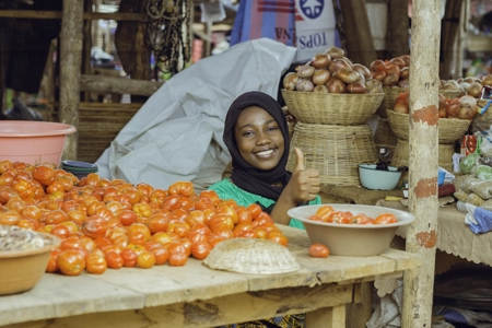 Une vendeuse souriante levant le pouce devant sa marchandise de tomate fraîches