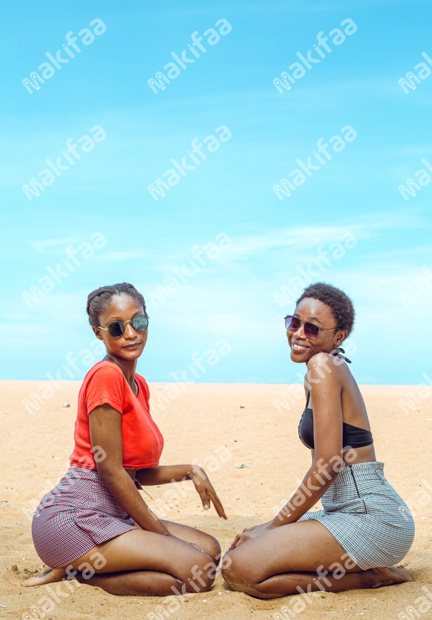 deux sœurs assises dans le sable portant des lunettes de soleil