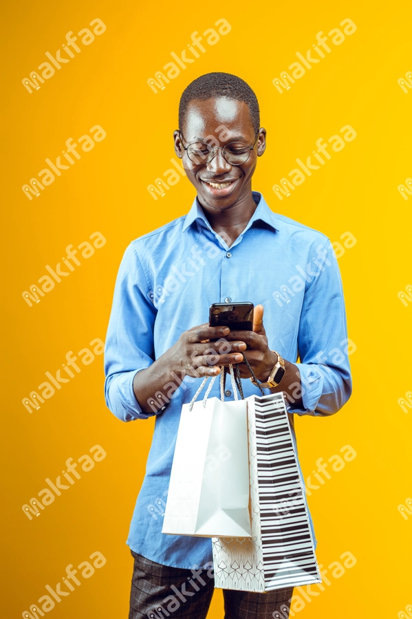 Homme souriant portant des avec son téléphone et des sacs de shopping