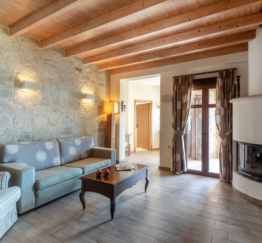 The interior of the residence with the modern fireplace, the table and chairs, the white walls and wooden ceiling