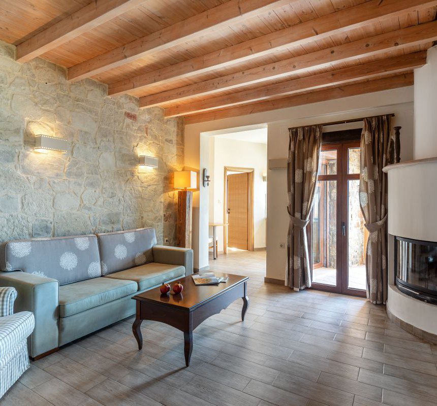 The interior of the maisonette with the stone walls, modern lights, balcony doors, the sofa, coffee table and fireplace