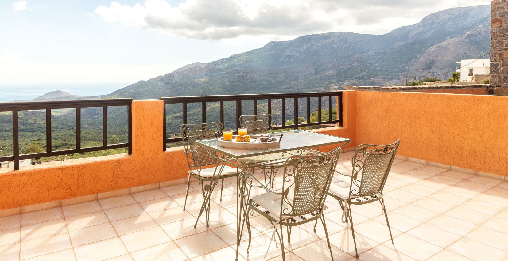 The interior of the Thyme residence of Mala Villa with the bed and the curtains around it, the bedside tables, the modern lights and the balcony with the view of the mountains in the background