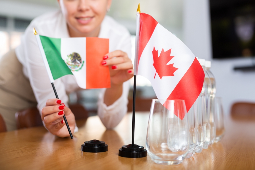 Woman in business clothes puts flags of Mexico and Canada
