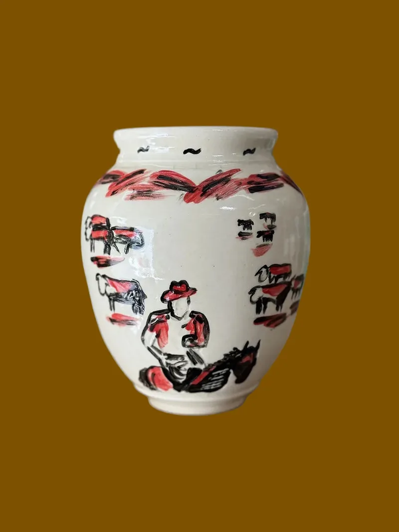 A cream-colored clay vase with hand-carved cows and floral patterns, with a predominantly red underglaze.