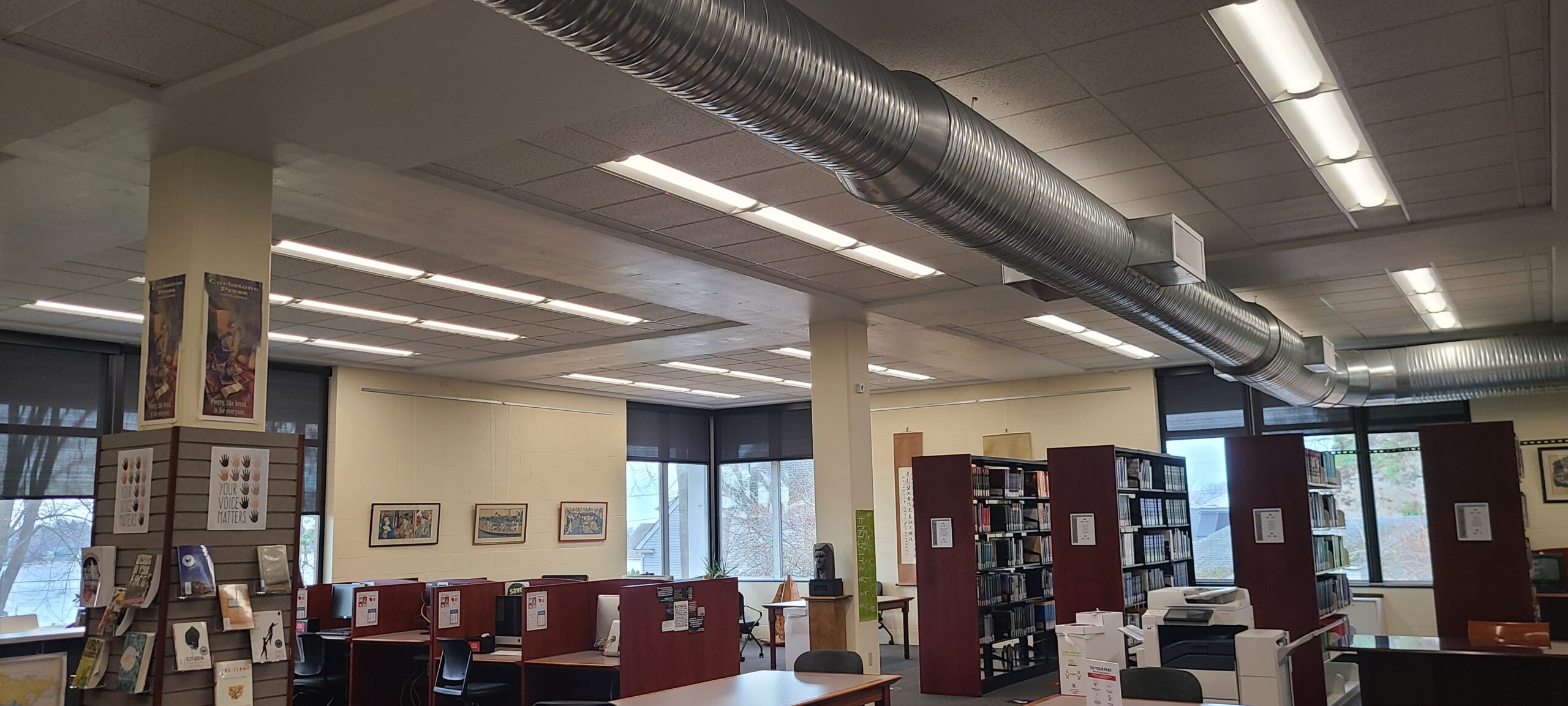 Mitchell College sustainability project as demonstrated through this image of LED lighting installed in their library above brown bookshelves and duct work in the ceiling