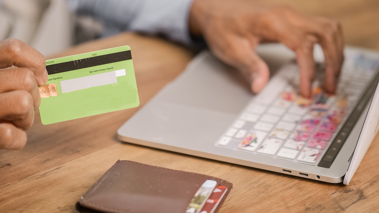 A hand holding a credit card and typing on laptop