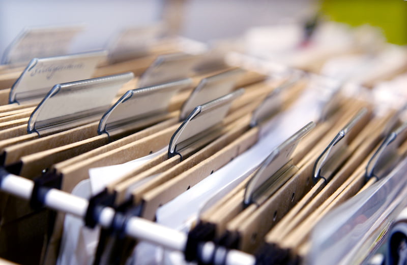 Close-up of organized file folders with metal tabs and labels on wooden shelves