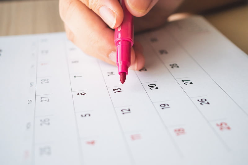 Hand holding pink marker marking dates on calendar for scheduling