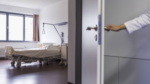 Eine Hand öffnet eine Tür zu einem leeren Bett in einem Krankenzimmer in einem Krankenhaus (Foto: IMAGO, imago/allOver-MEV)