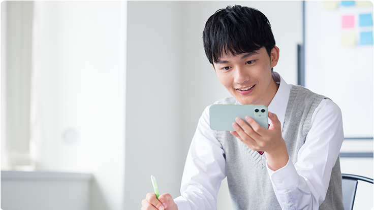 スマートフォンで講義動画を見ながらペンを持って学習する受講生