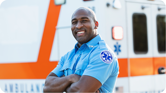 A paramedic standing in front of an ambulance, looking at the camera. He is an African-American man in his 30s