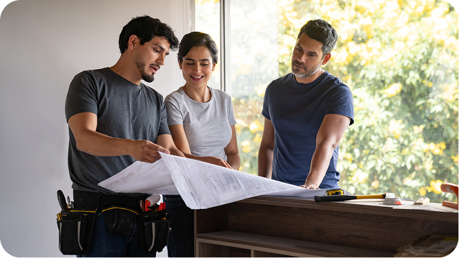 Three adults, two men and one woman, reviewing blueprints together in a bright room with a large window.