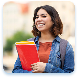Young woman with shoulder-length dark hair smiling brightly while standing outdoors, wearing a blue denim jacket over a rust-colored shirt. She is holding a bright red notebook or textbook and appears to be in an academic or campus setting with a blurry background. Her expression is joyful and confident, radiating positivity and enthusiasm. She carries a backpack, suggesting she is a student. The image captures a candid moment of academic energy and personal happiness, with soft natural lighting highlighting her warm, genuine smile.