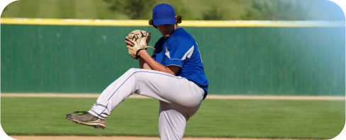 Teenager pitcher in a blue shirt preparing to throw the ball in a baseball game