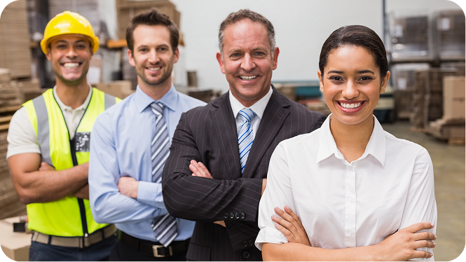 Here are a few options for the image's alt text, depending on how and where you plan to use it on your website to ensure ADA/accessibility compliance:  Option 1: Standard & Descriptive (Recommended) alt="A diverse warehouse team of four smiling and standing together with their arms crossed, including a worker in a hard hat and safety vest alongside managers in business attire.