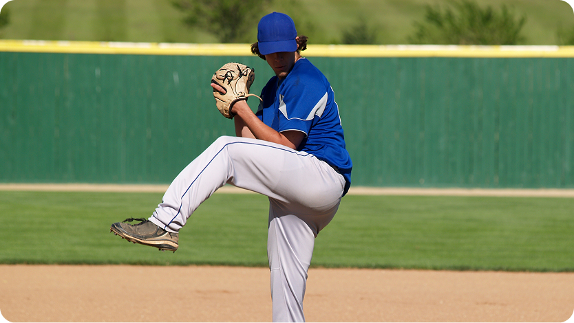 Youn pitcher in a blue baseball shirt preparing to throw a ball in a baseball game